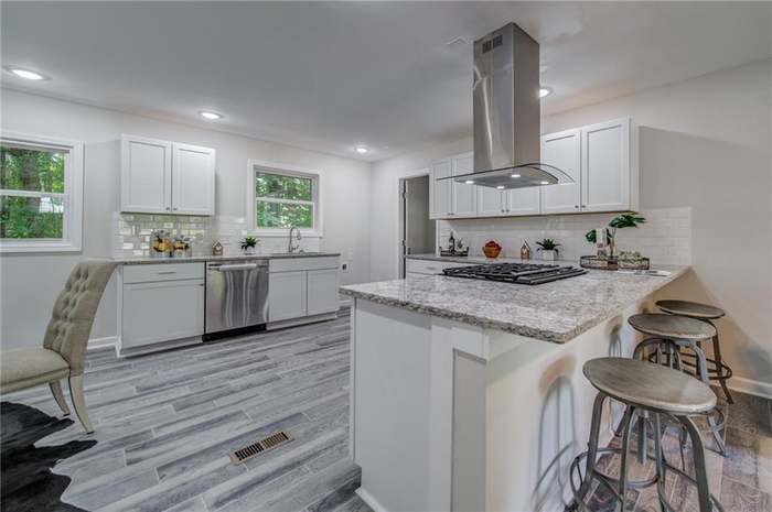 Open-concept kitchen with white cabinets, granite island, and stainless range hood